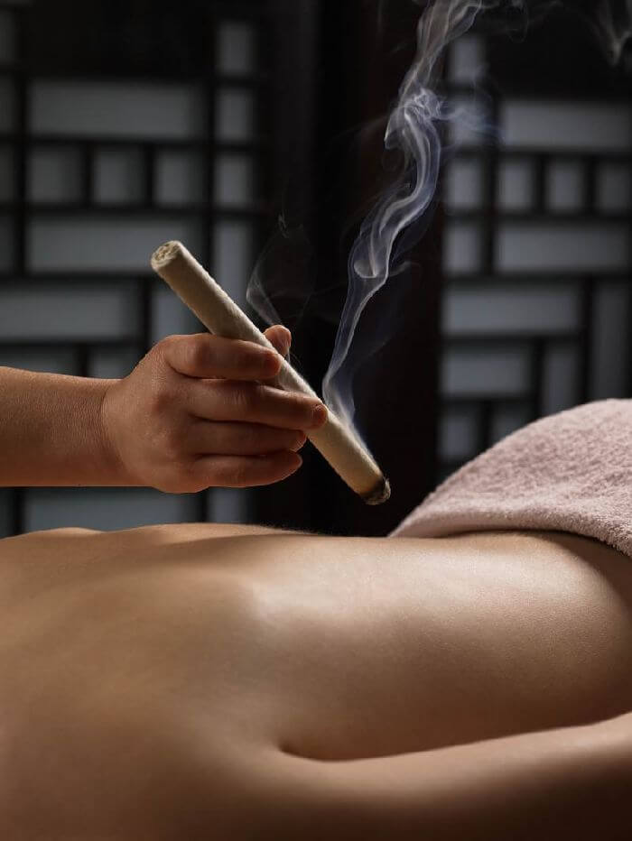 Moxibustion stick warming the lower back at MIRA Integrative Clinic